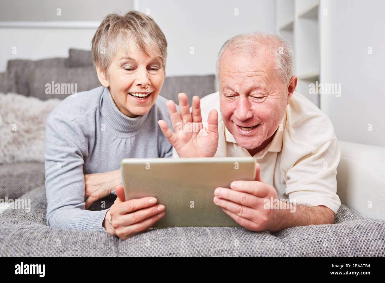Happy senior couple having video chat with tablet computer in living room Stock Photo