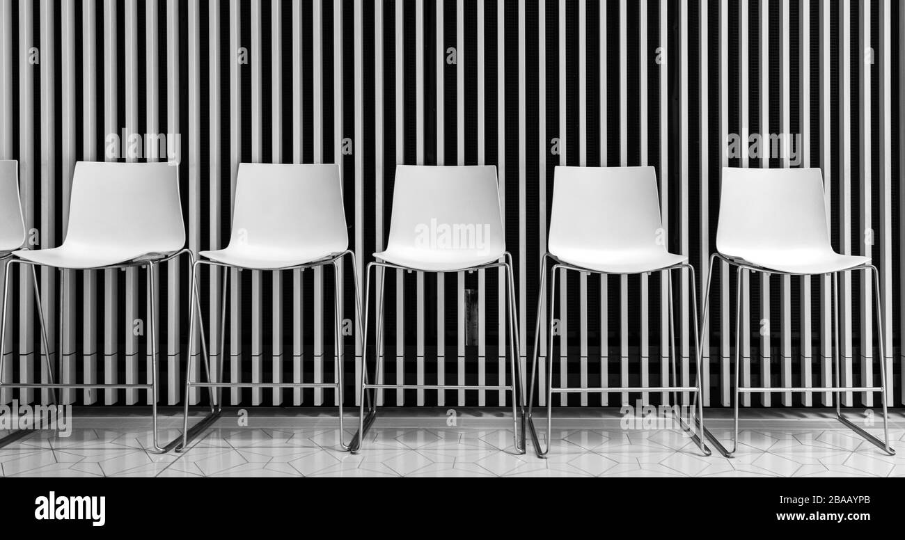 white plastic bar stools stand in front of a structured wall Stock Photo