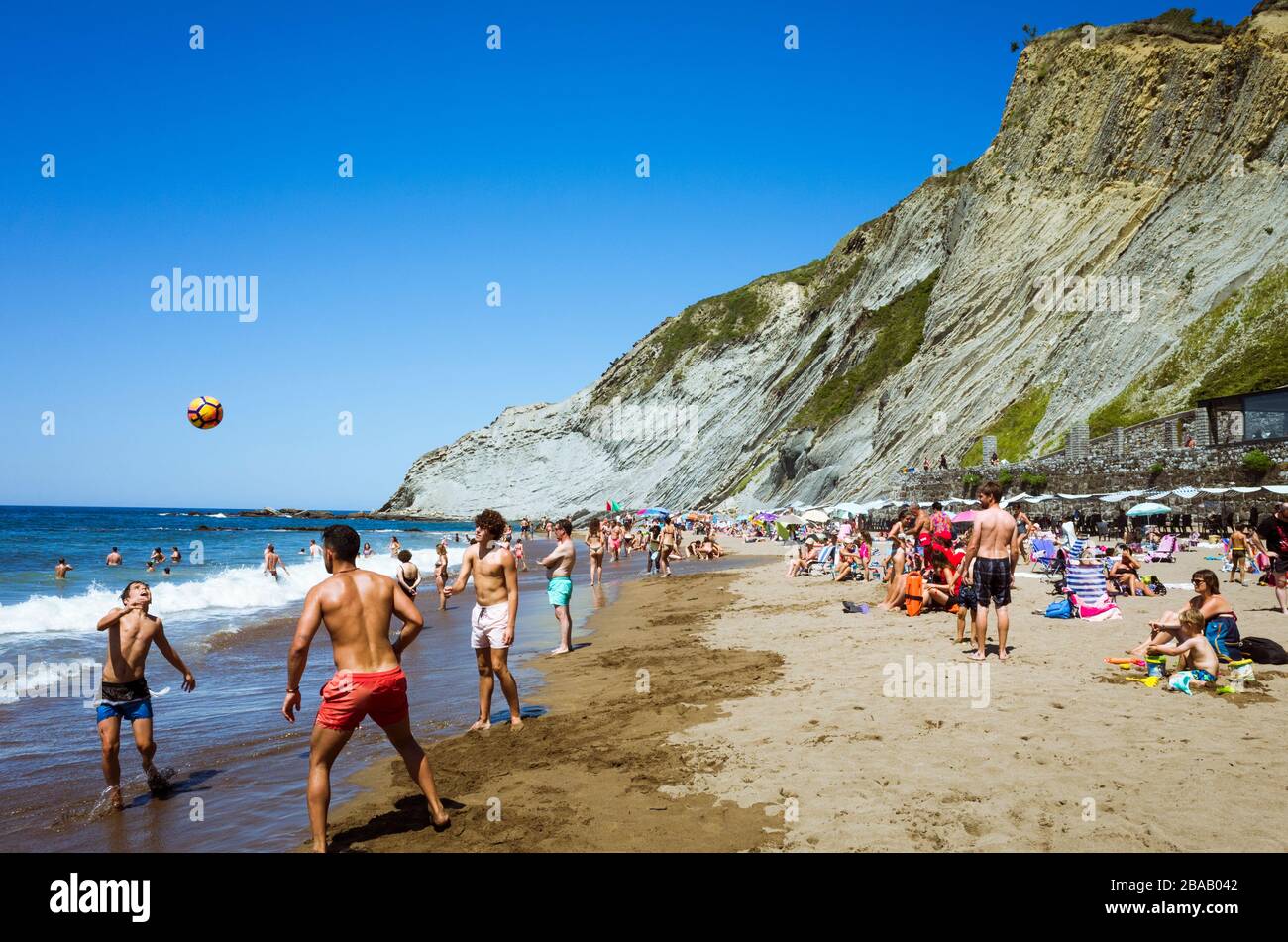 Zumaia, Gipuzkoa, Basque Country, Spain - July 15th, 2019 : Beach goers play ball on the shore at Itzurun Beach. Stock Photo