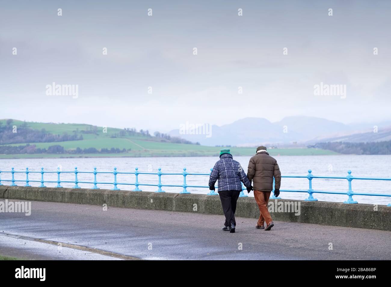 Senior couple daily walk at sea esplanade during rain storm in cold months Stock Photo