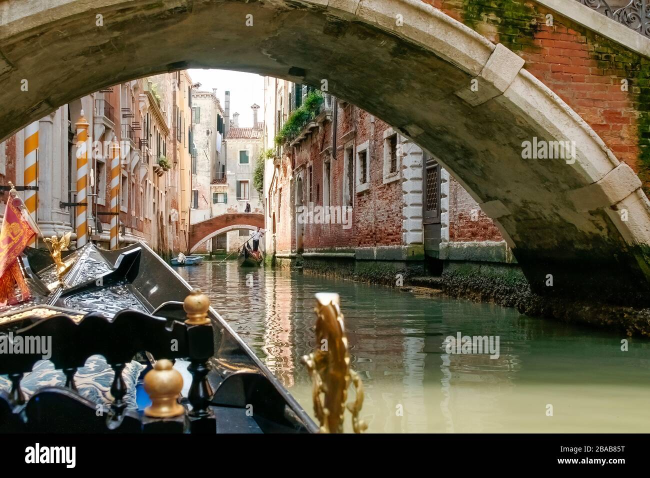 View while riding in a gondola. Passing under one of the traditional arched bridges with buildings on both sides and another gondola coming Stock Photo