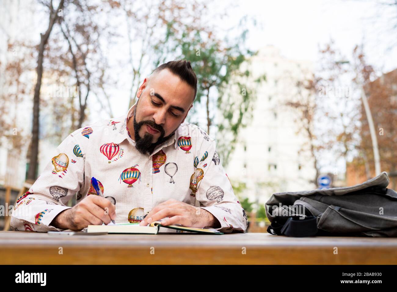 Bearded man sitting outdoors while working over a wooden table Stock Photo