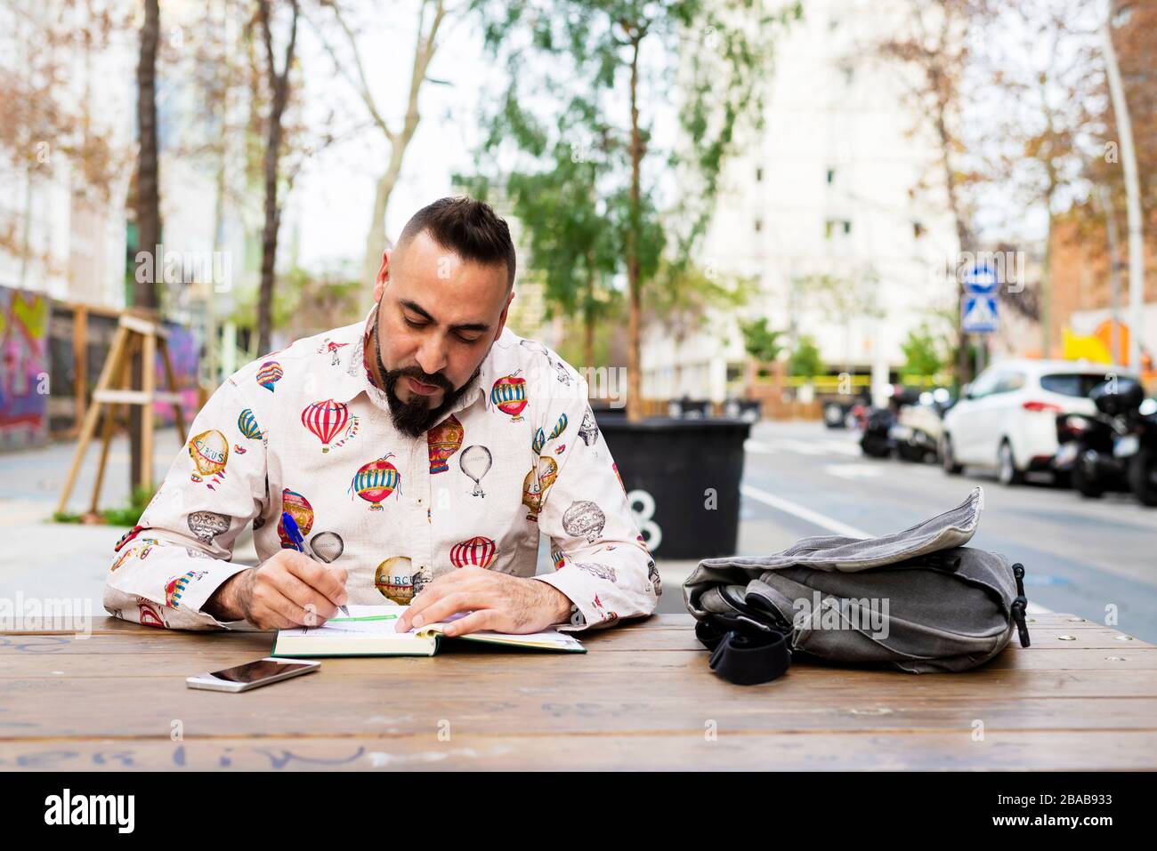 Bearded man sitting outdoors while working over a wooden table Stock Photo