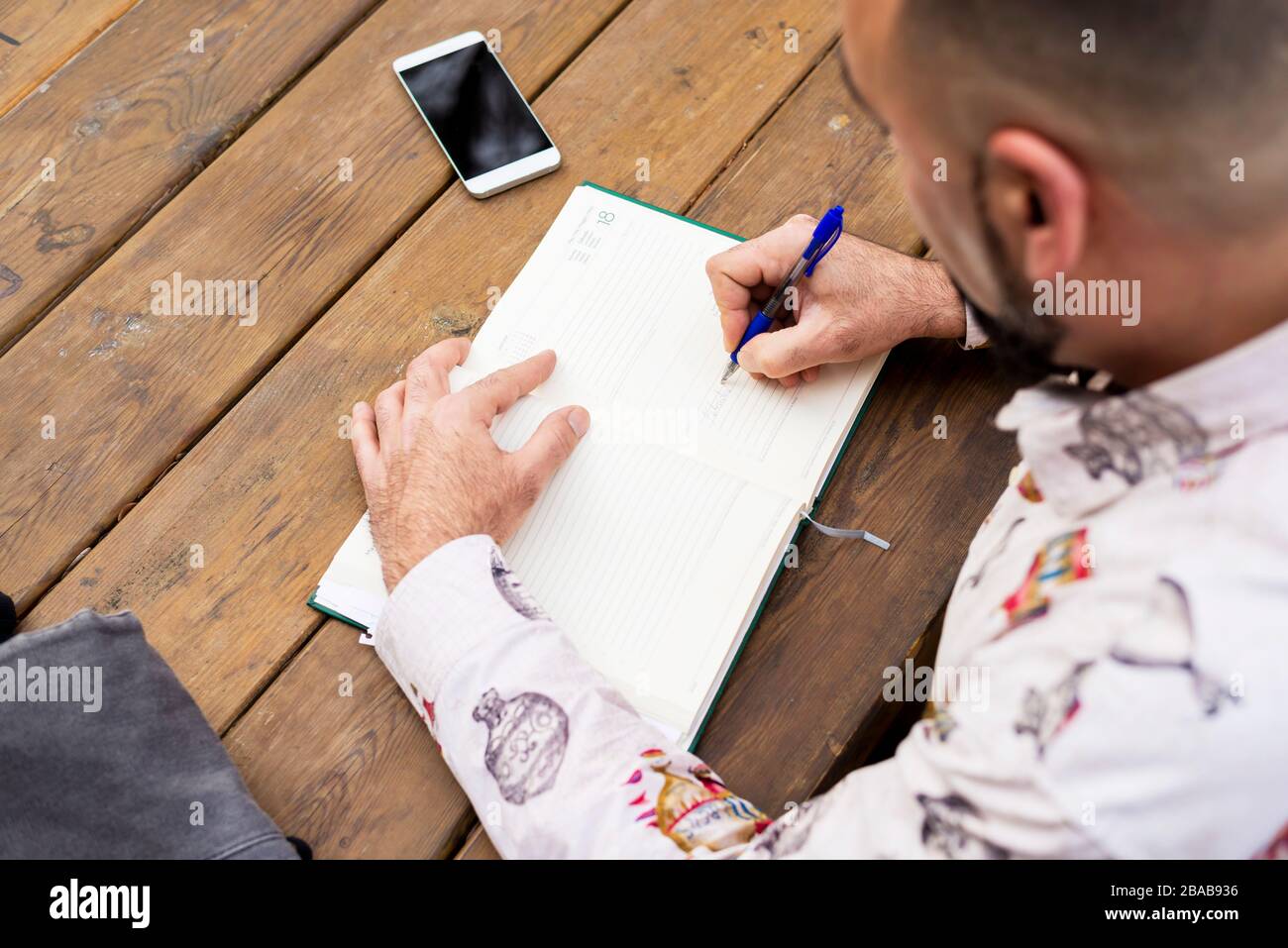 Young bearded businessman sitting at table, making notes in notebook Stock Photo