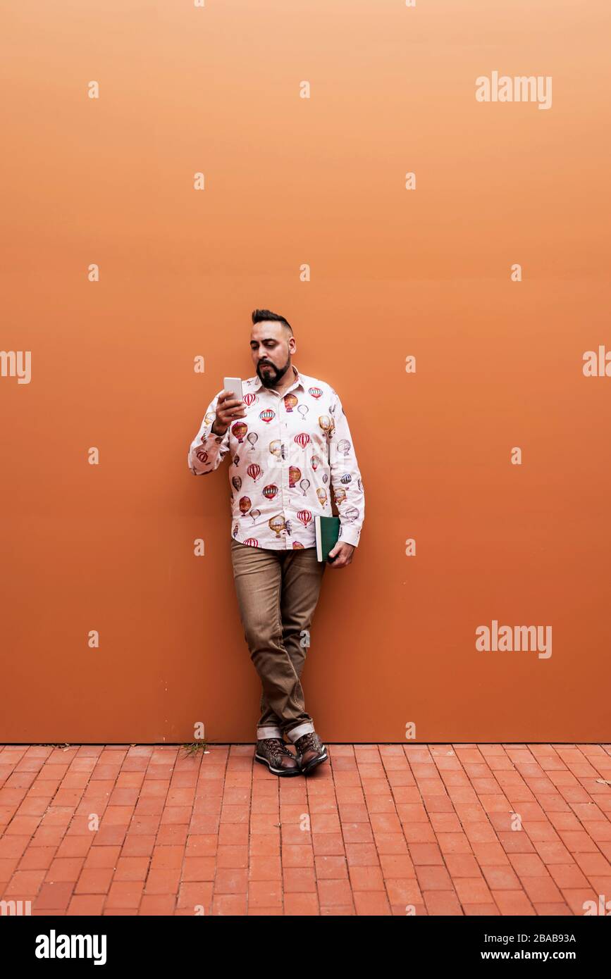 Bearded man leaning on wall while using smartphone by office building Stock Photo