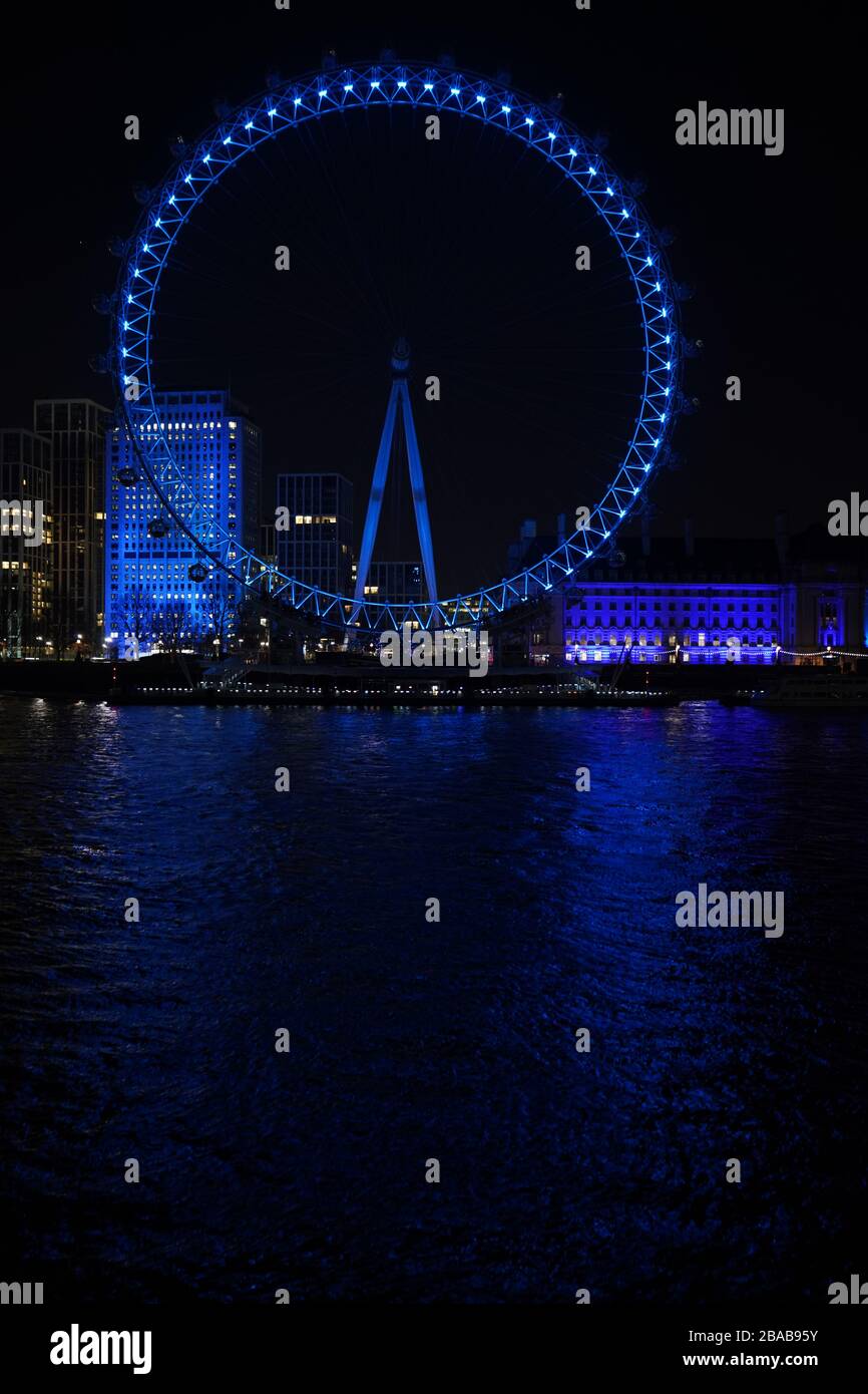 The London Eye and County Hall in London are lit up in blue in a gesture of thanks to the hardworking NHS staff who are trying to battle coronavirus. A national salute for the frontline healthcare heroes is taking place across the UK with a mass round of applause from doorsteps, windows and balconies on Thursday at 8pm. Stock Photo