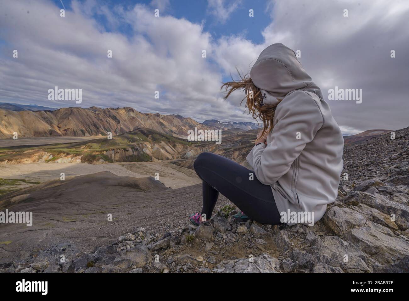Woman sitting on top of mountain in the wind, in Landmannalaugar Stock Photo