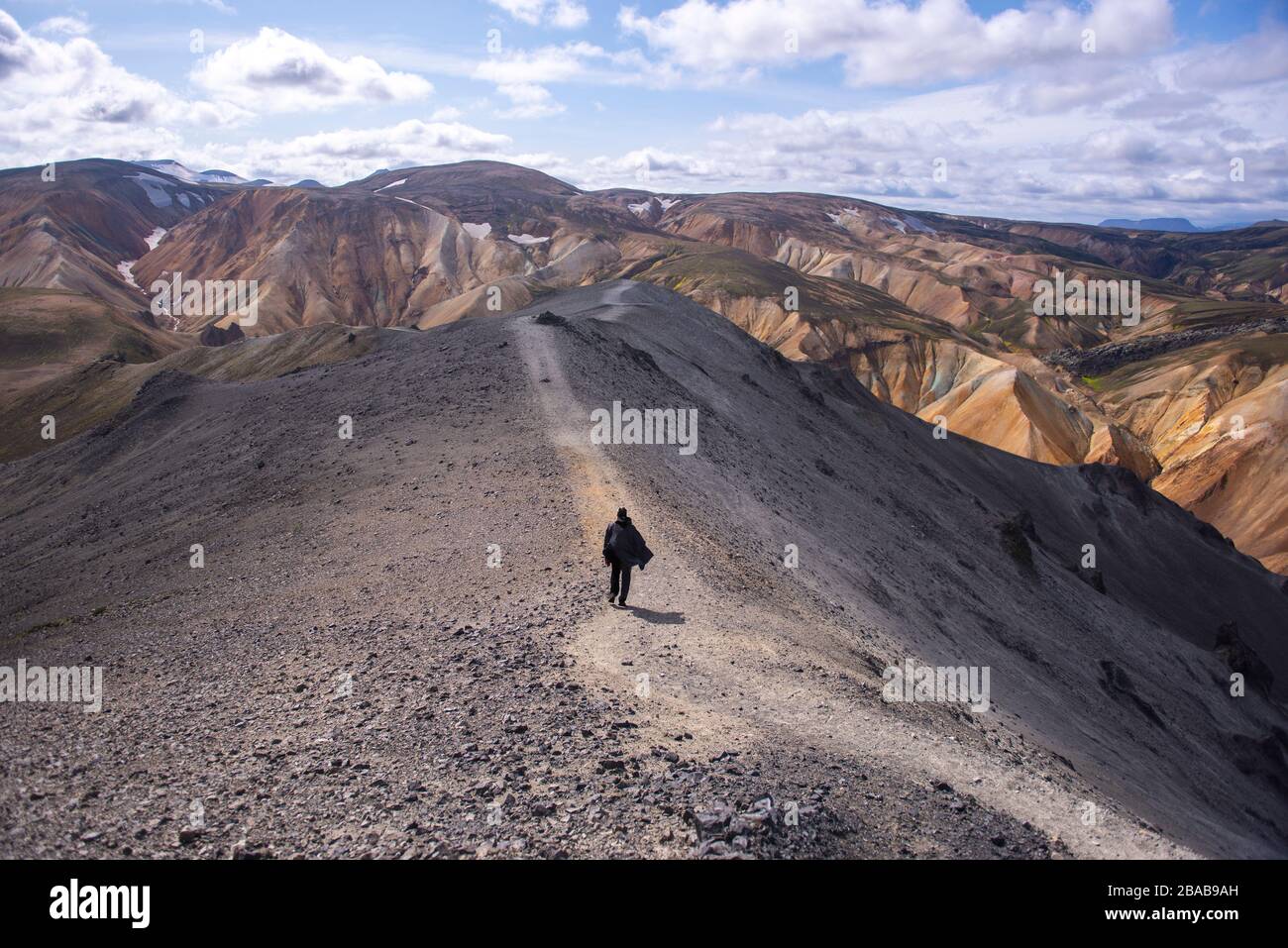 Man with cape walking down trail on top of mountain in Iceland Stock Photo
