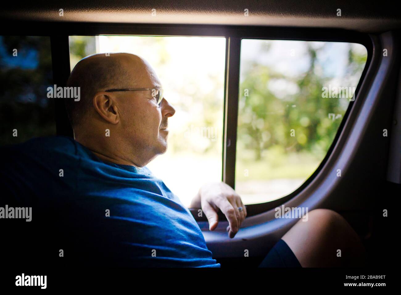 Relaxed retired man sits next to window in back of vehicle. Stock Photo