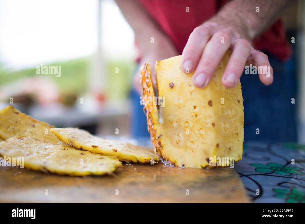 Detailed view of man slicing fresh pineapple outdoors Stock Photo