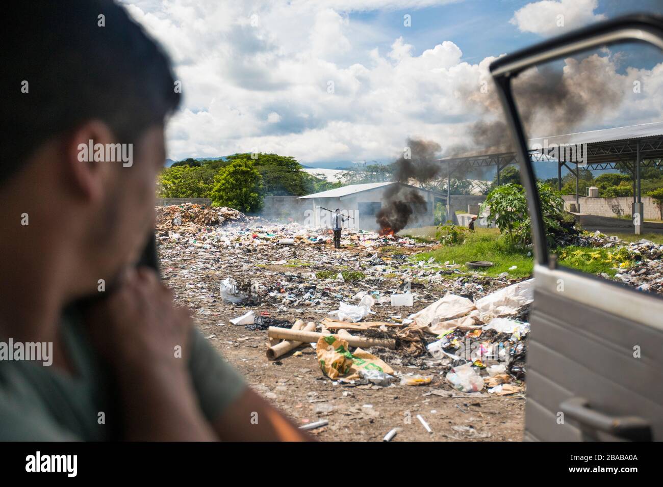 View from vehicle of worker at dump burning garbage. Stock Photo