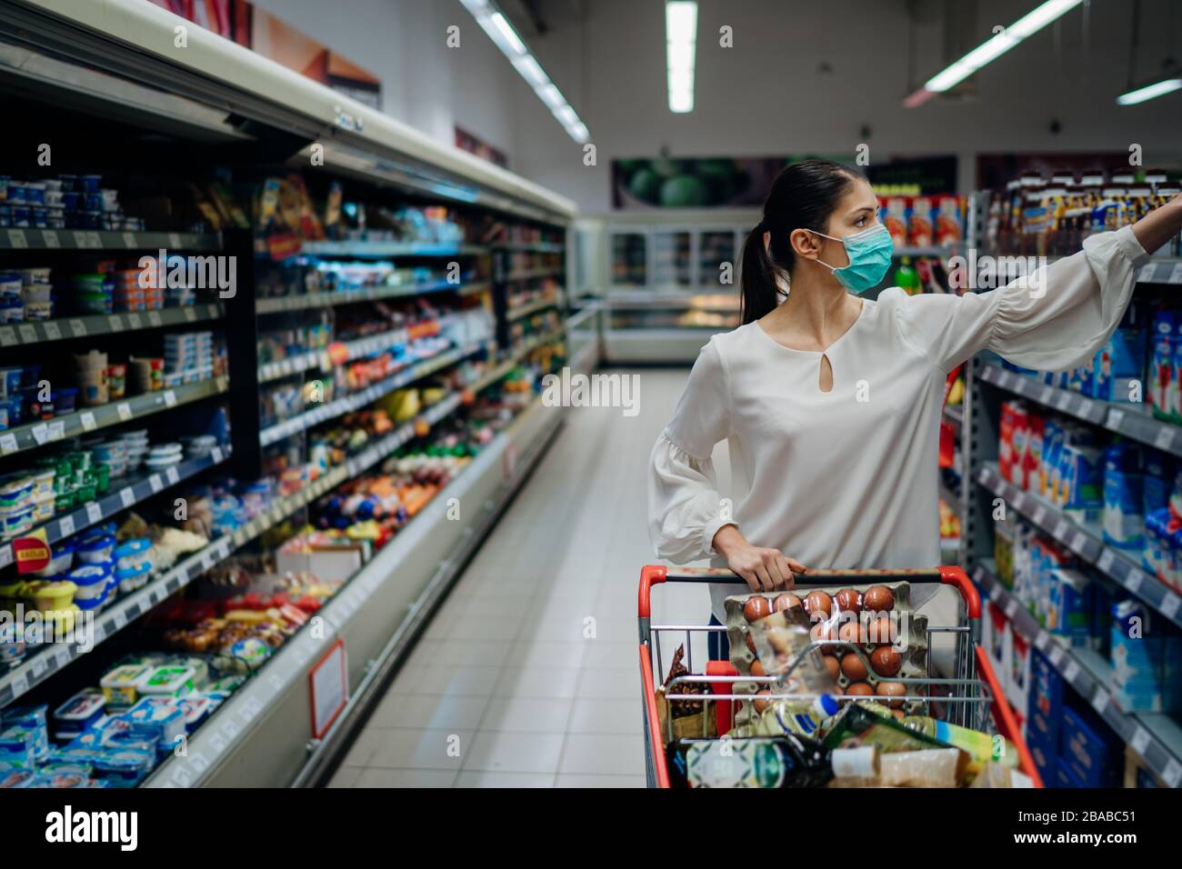 Woman with hygienic mask shopping for supply.Budget buying at a supply store.Emergency to buy list.Shopping for enough food and cleaning products.Prep Stock Photo