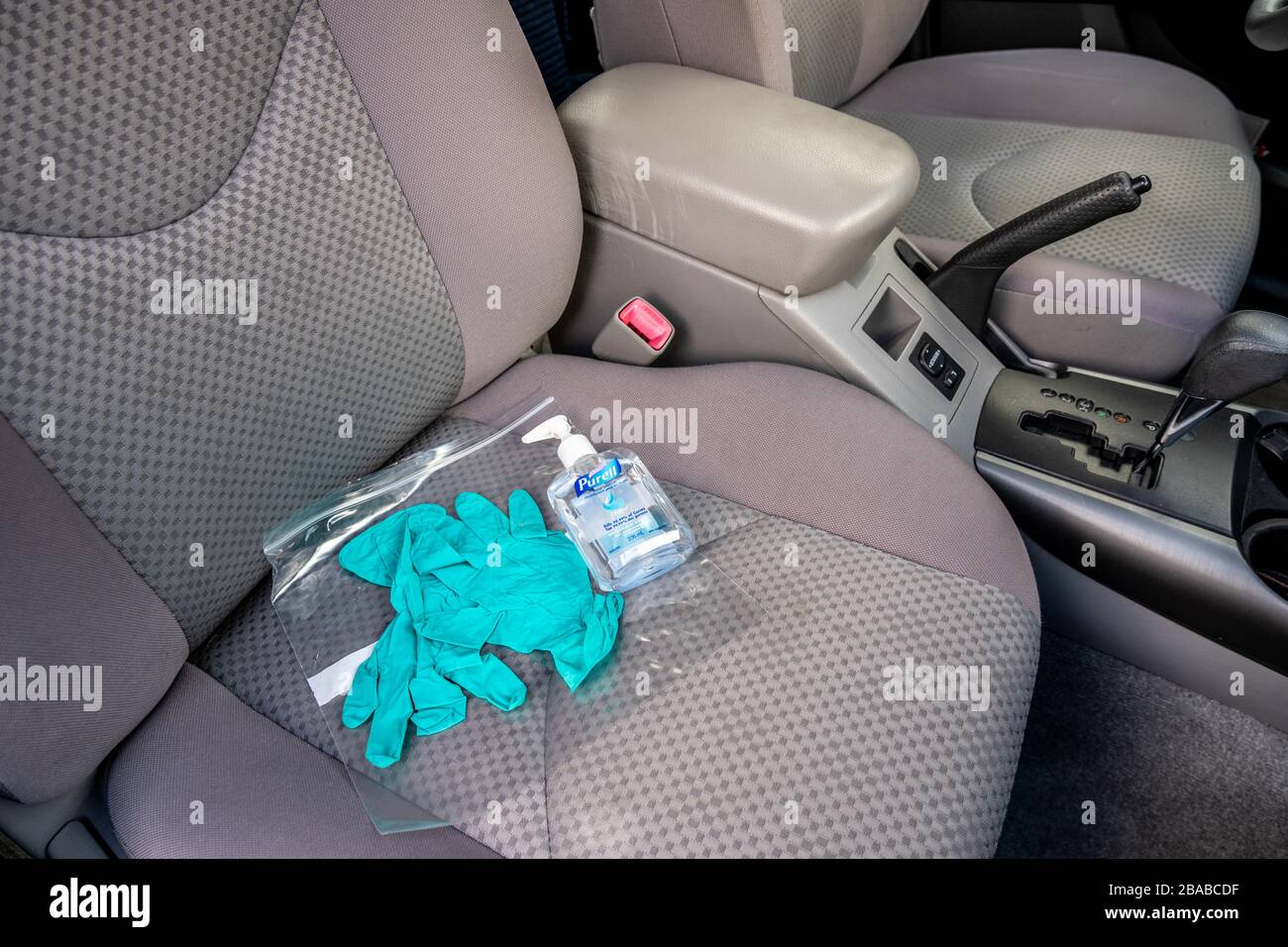 Surrey, Canada - March 25, 2020: Green nitrile disposable gloves and hand sanitizer with plastic bag on car seat during time of Coronavirus pandemic Stock Photo