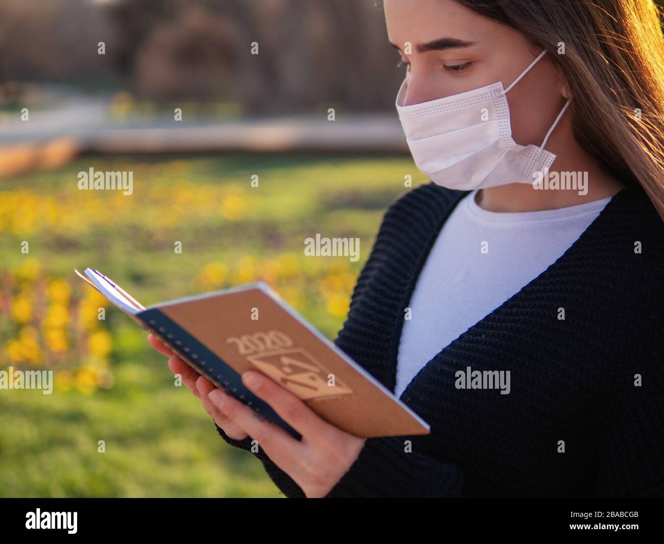 Beautiful woman in mask in side profile studing outdoors in the backyard of her home. Self distancing and quarantine concept. Young woman in mask read Stock Photo