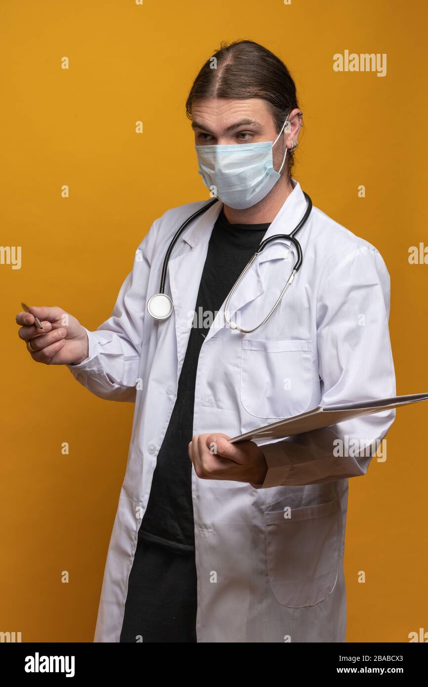 Young doctor with stethoscope, holding a map and a pen is explaining something to someone visible not in the frame due to a minimum 1.5m distance requ Stock Photo