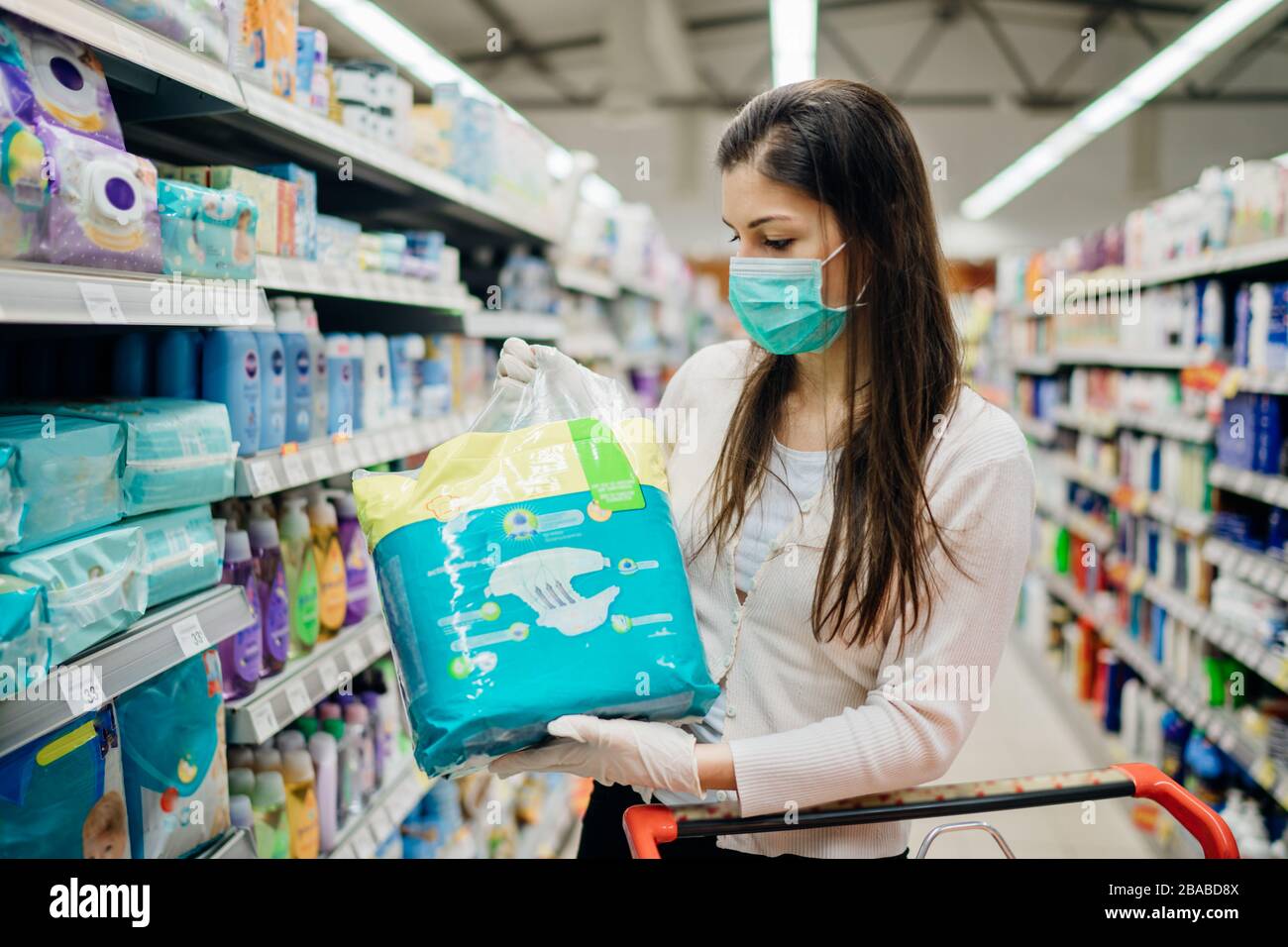 Woman shopper with mask and gloves panic buying disposable diapers.Preparing for pathogen virus pandemic quarantine.Prepper buying bulk baby products Stock Photo