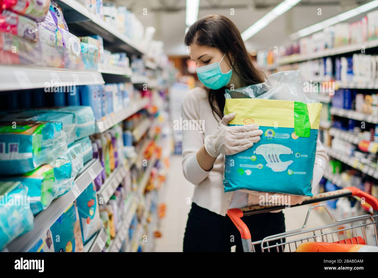 Woman shopper with mask and gloves panic buying disposable diapers.Preparing for pathogen virus pandemic quarantine.Prepper buying bulk baby products Stock Photo