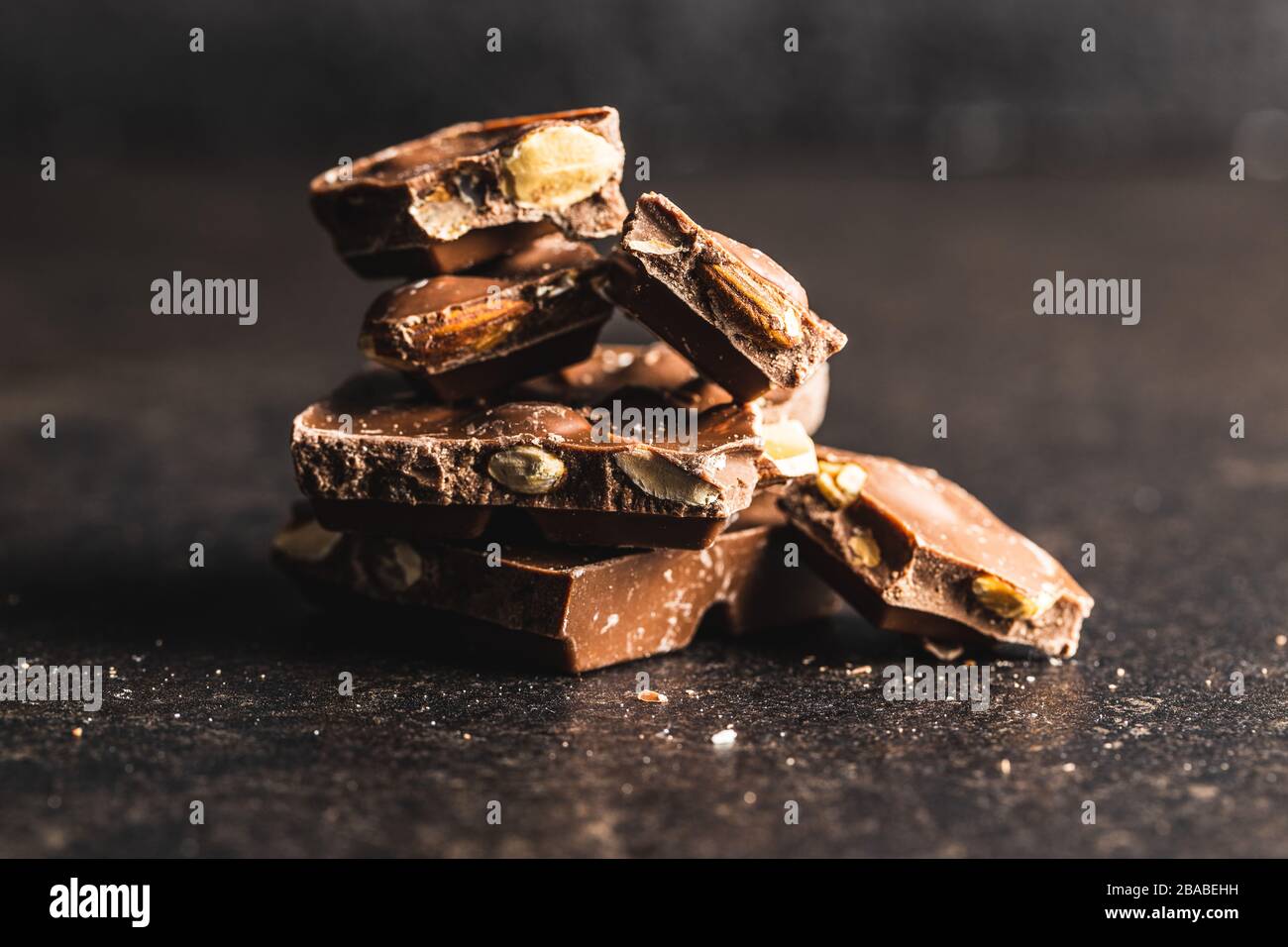 Dark nut chocolate. Broken chocolate bar on black kitchen table. Pile