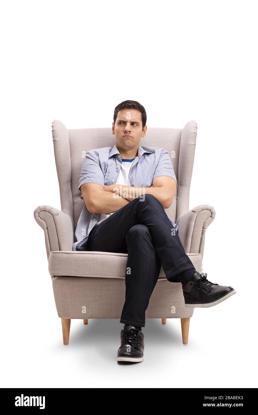 Angry young man making a grimace and sitting in armchair isolated on ...