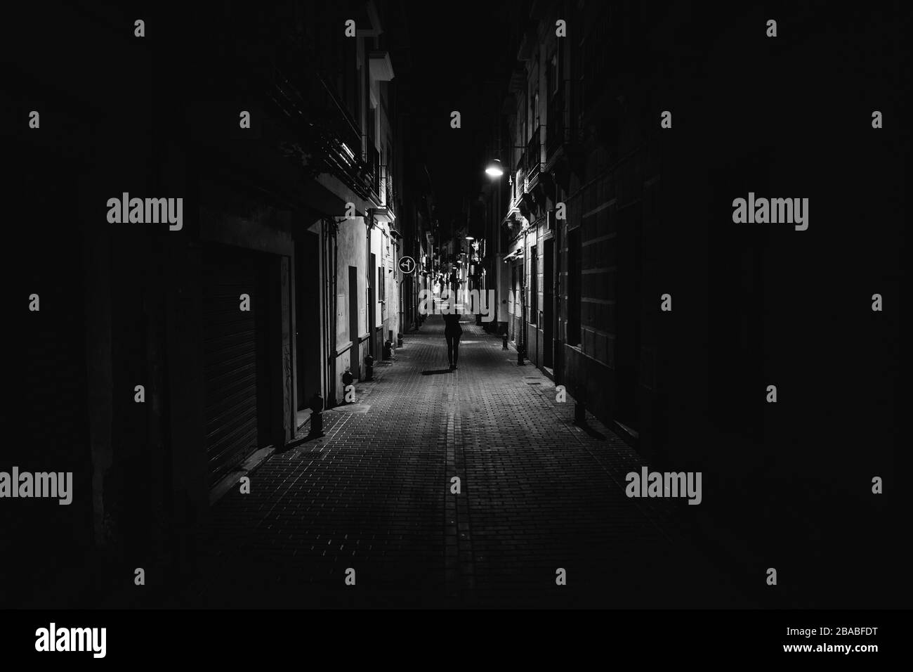 Women walking alone in the street late at night.Narrow dark alley, unsafe female silhouette.Empty streets.Woman pedestrian alone.Police hour.Assault Stock Photo