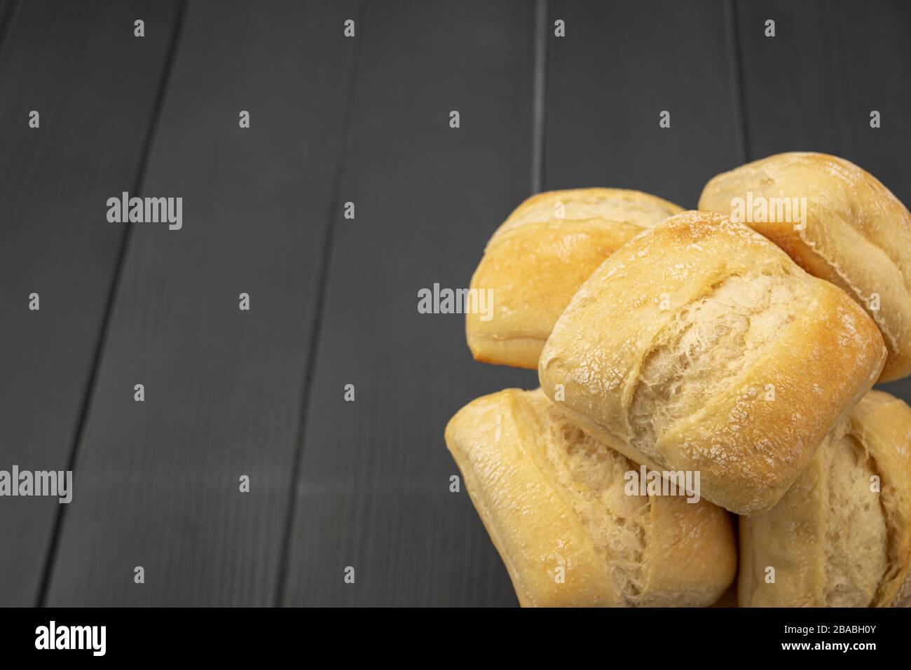 Heap of freshly baked and golden bread ready for consumption on gray wooden table with light traces of flour Stock Photo