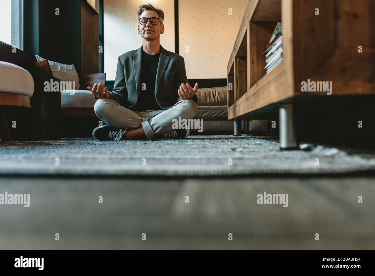 Low angle shot of a mid adult businessman doing yoga meditation. Business professional meditating in yoga pose in office lounge area. Stock Photo
