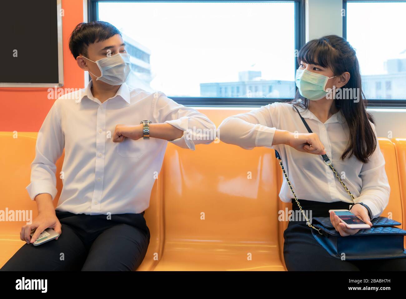 Elbow bump is new novel greeting to avoid the spread of coronavirus. Two Asian business friends meet in subway. Instead of greeting with a hug or hand Stock Photo