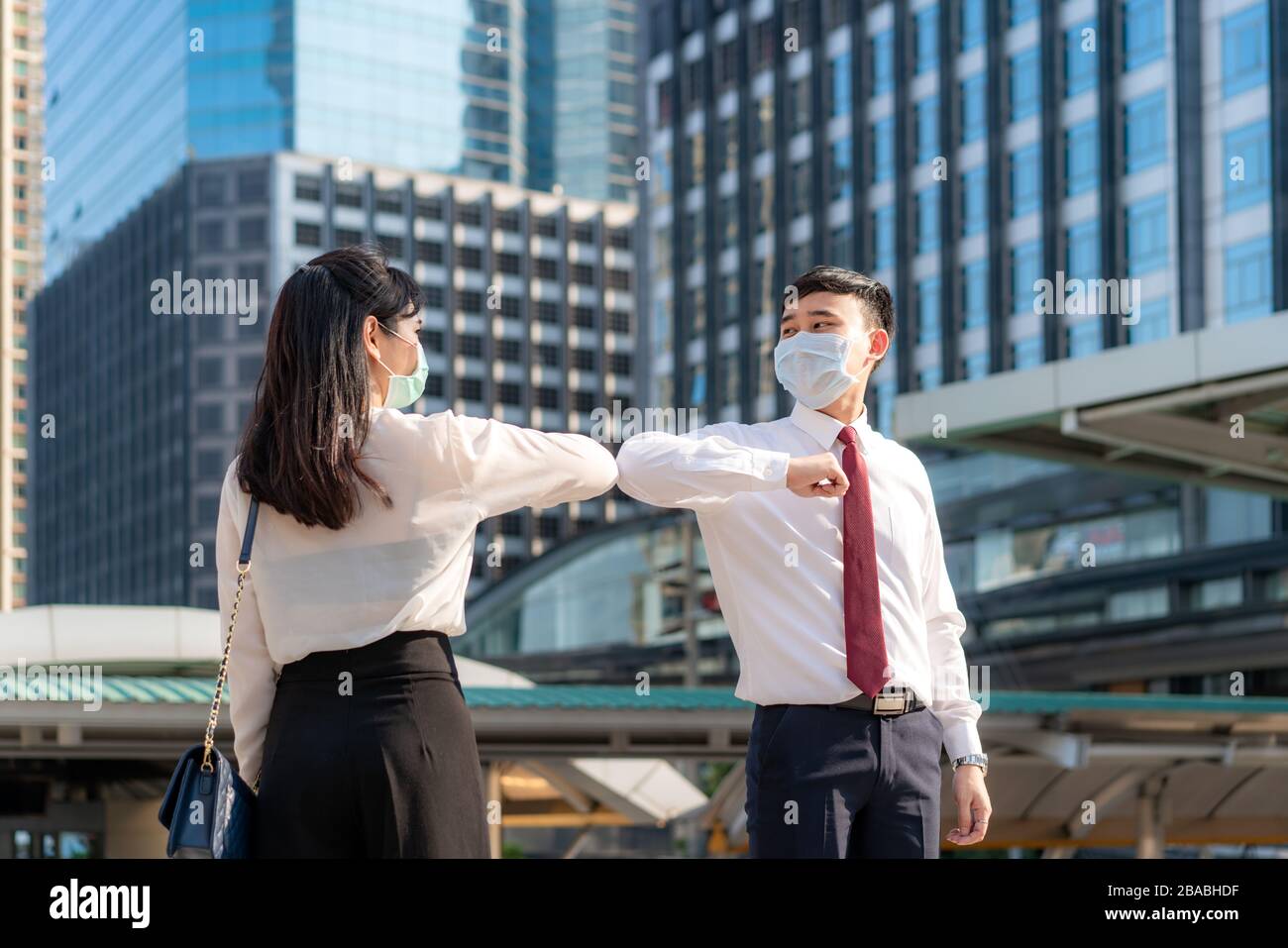 Elbow bump is new novel greeting to avoid the spread of coronavirus. Two Asian business friends meet in front of office building. Instead of greeting Stock Photo