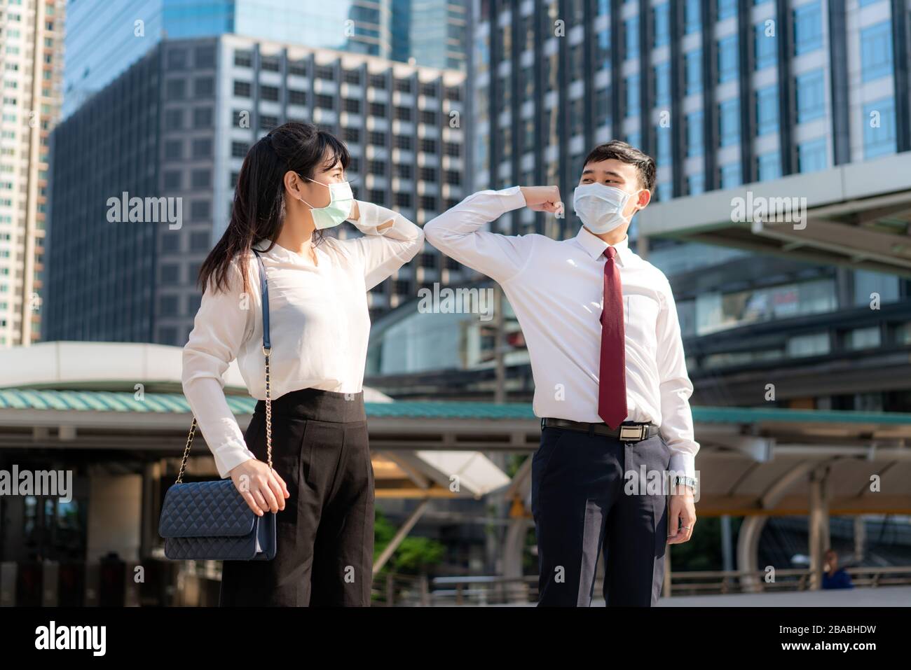 Elbow bump is new novel greeting to avoid the spread of coronavirus. Two Asian business friends meet in front of office building. Instead of greeting Stock Photo