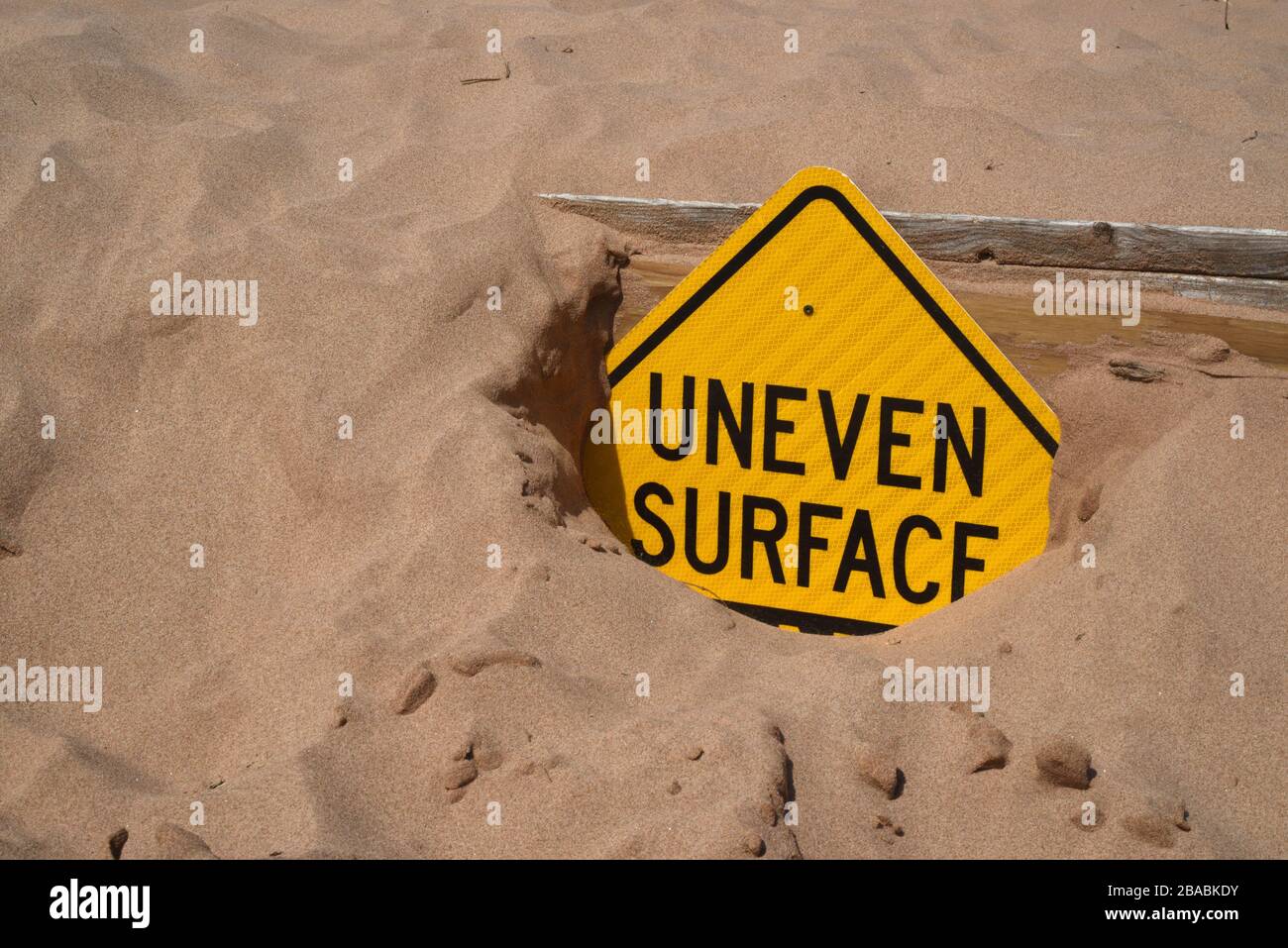 A sign half buried in shifting sand warns of Uneven Surface at Cavendish Beach in Prince Edward Island, Canada Stock Photo