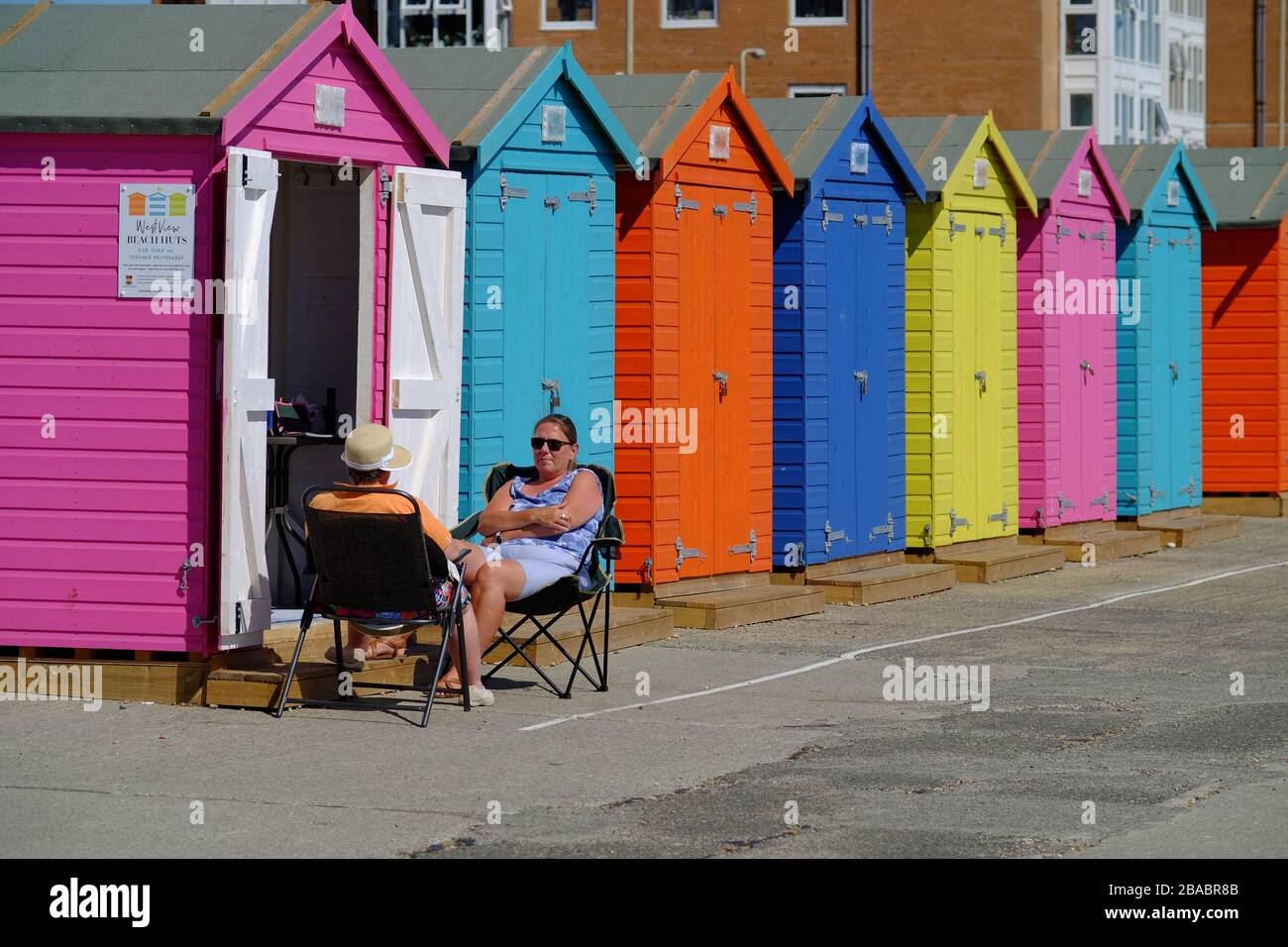 Couple relaxing by colourful beach huts, Seaford, UK Stock Photo