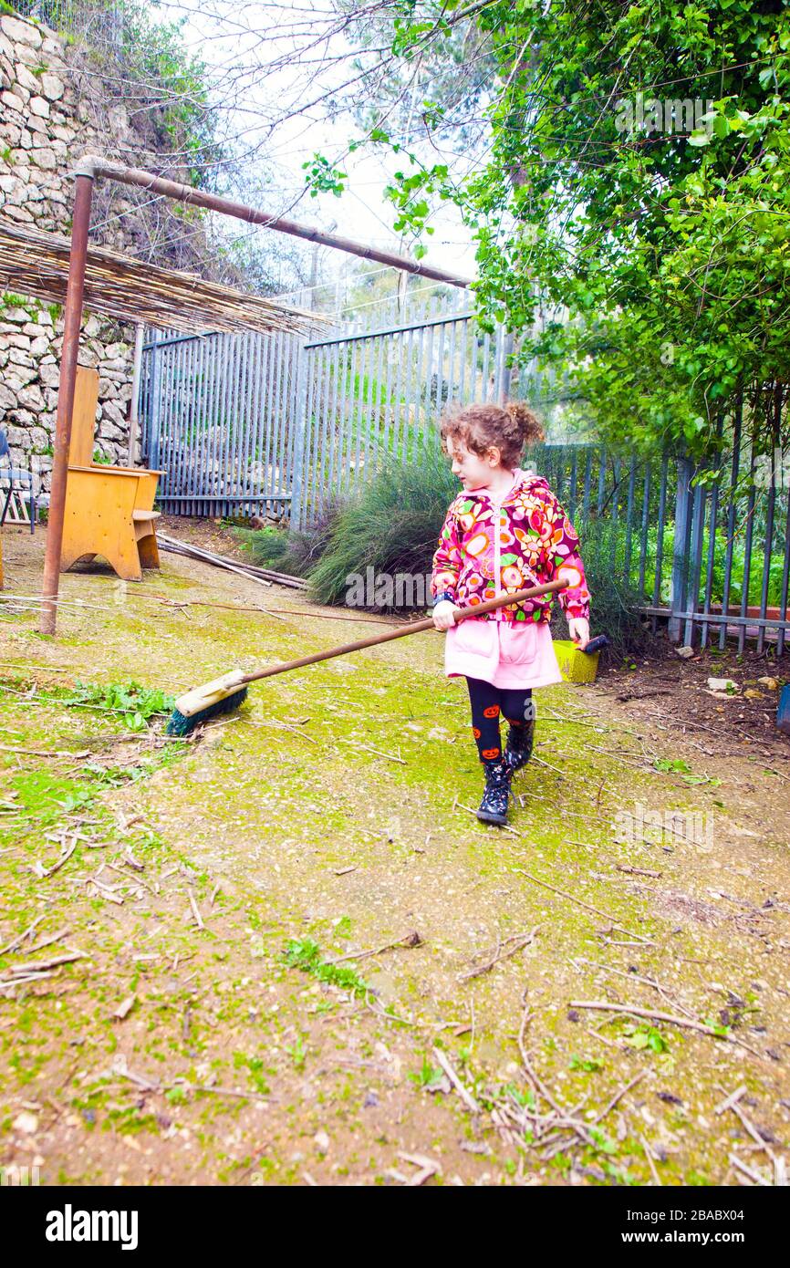 Little girl with a broom helps clean the house backyard Stock Photo