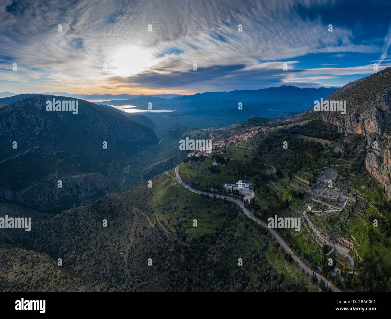 Aerial view of Delphi, Greece, the Gulf of Corinth, orange color of clouds, mountainside with layered hills beyond with rooftops in foreground Stock Photo