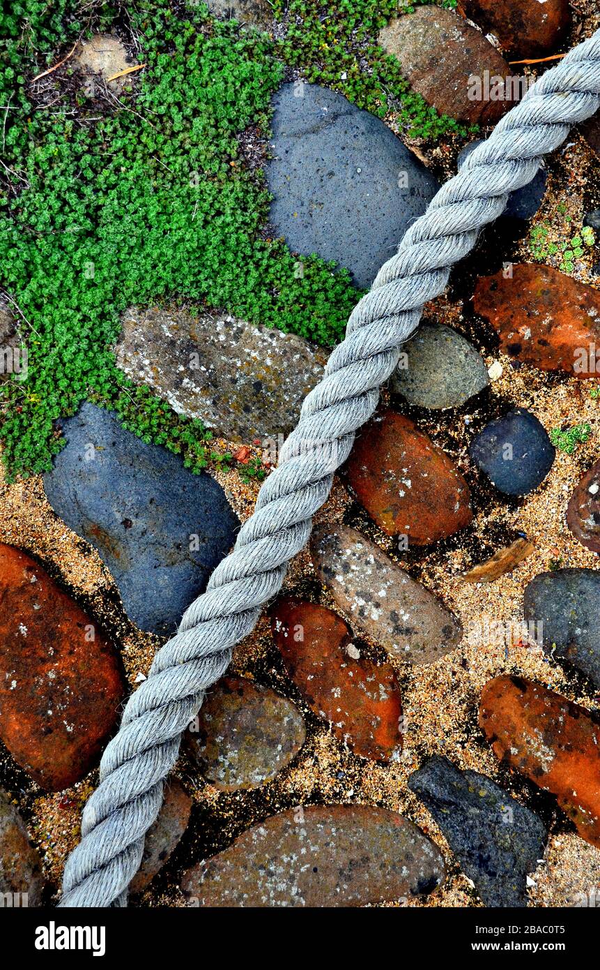 old colorful cobble stones and low lying weeds with blue boat rope Stock Photo