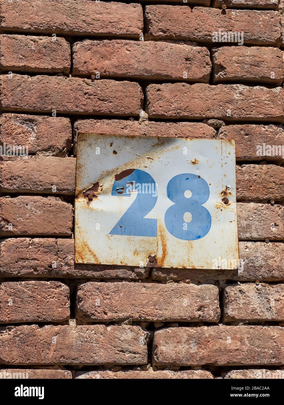 Street number 28 on a metal placard against a brick wall, blue numbers on a white background Stock Photo
