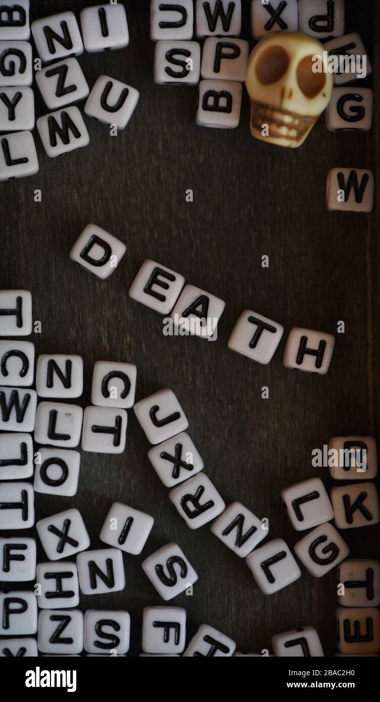Still life showing black and white letter blocks spelling out the word death among other letter blocks and a skull against a black background Stock Photo