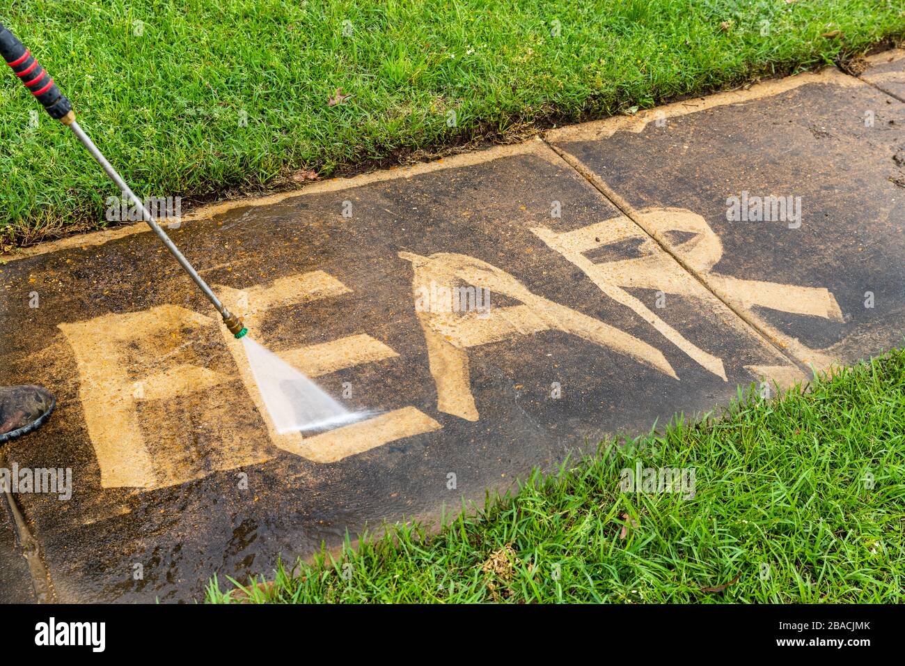 The word 'Fear,' on a sidewalk, being erased with a pressure washer Stock Photo