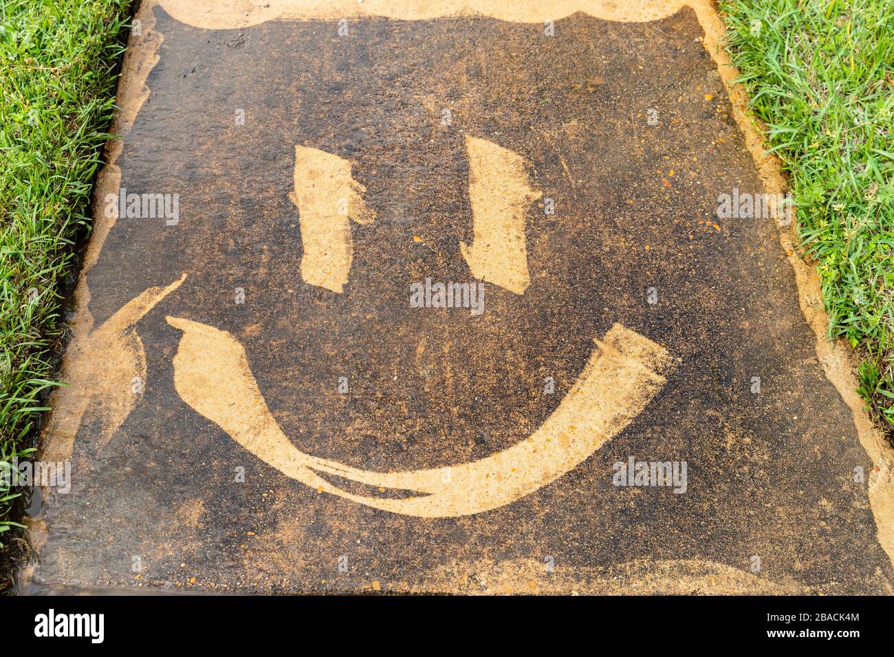 A smiley face created on a dirty sidewalk with a pressure washer Stock Photo