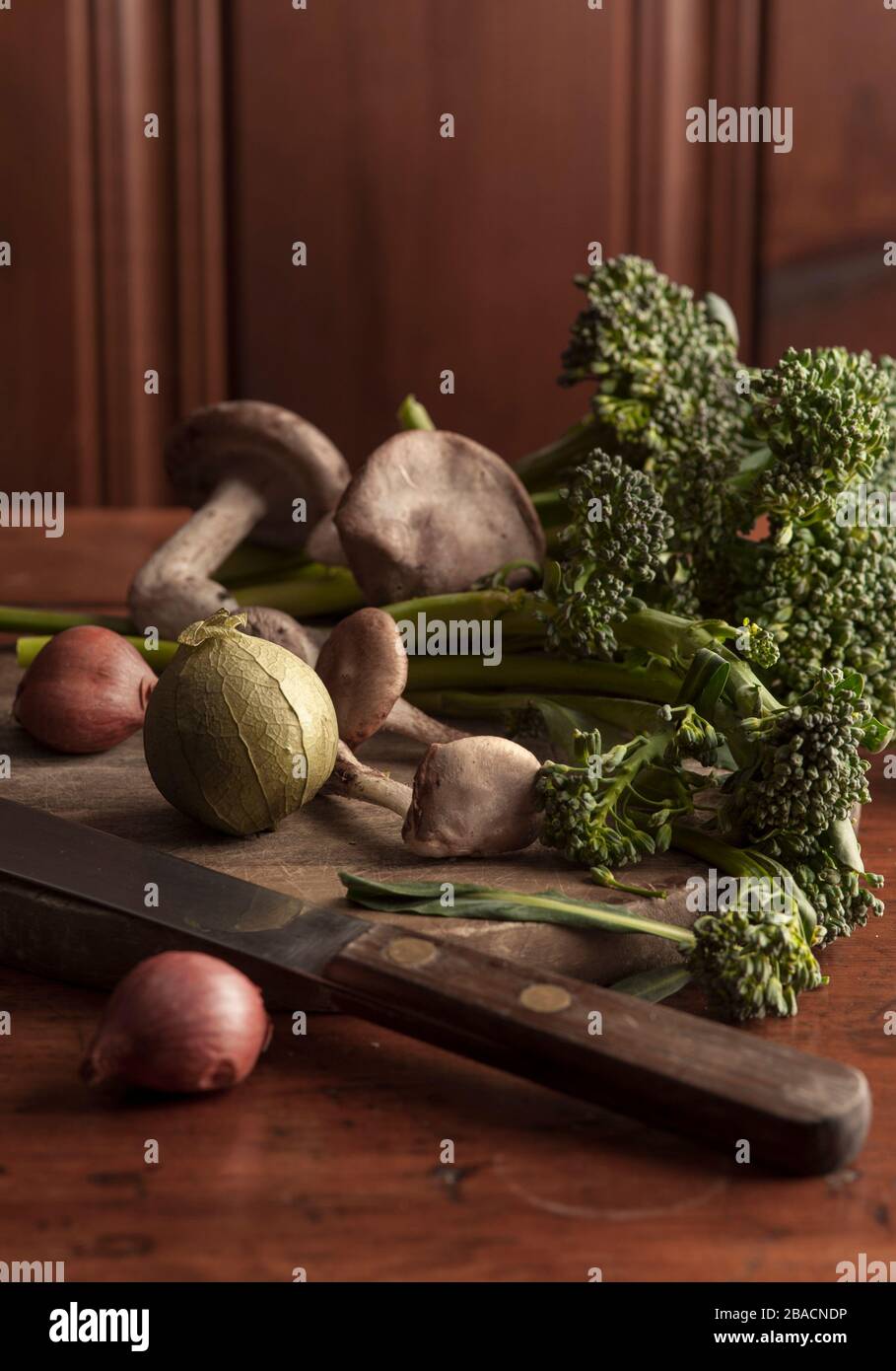 Still life of mushrooms, shallots, broccolini and tomatillo onwood cutting board. Stock Photo