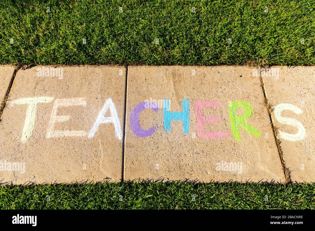 The word "Teachers" written with sidewalk chalk, on gray concrete pavement background. Stock Photo