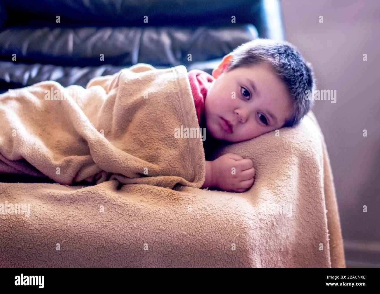 sick little boy rests in big chair with his blanket Stock Photo