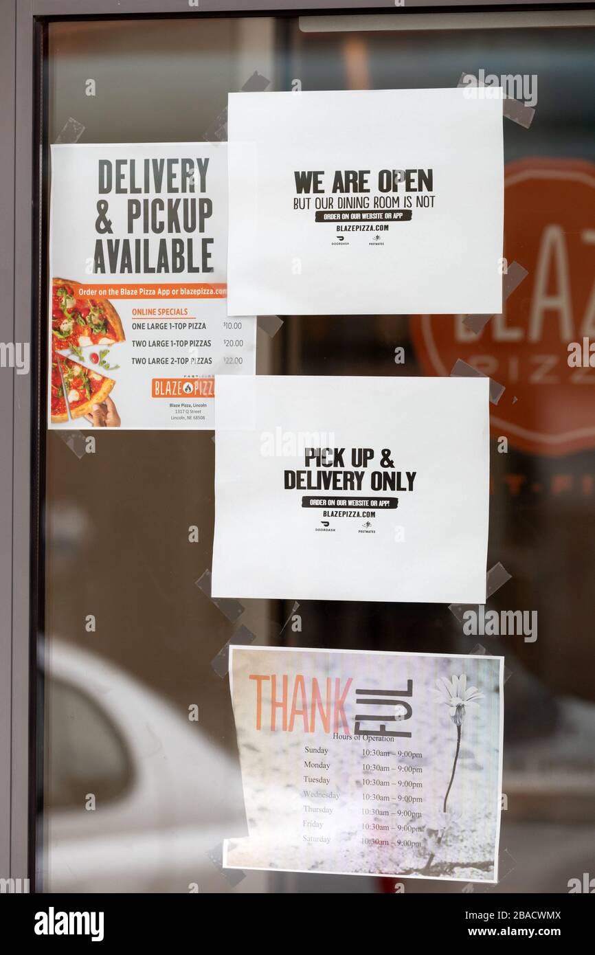 Signs on a window stating that a pizza business is open but allowing only take-out or delivery dining due to COVID-19. Stock Photo