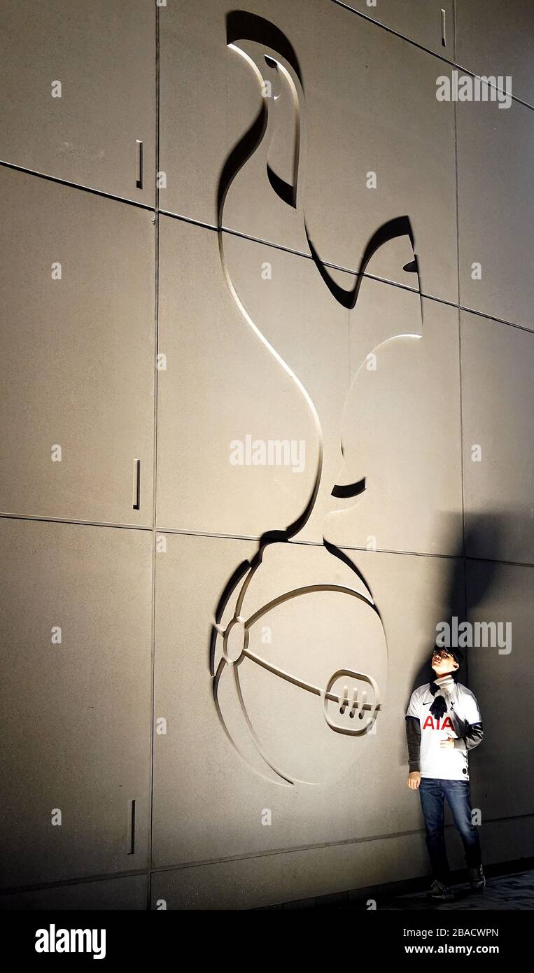 A Tottenham Hotspur fan poses for a picture in front of the club crest on the side of the stadium Stock Photo