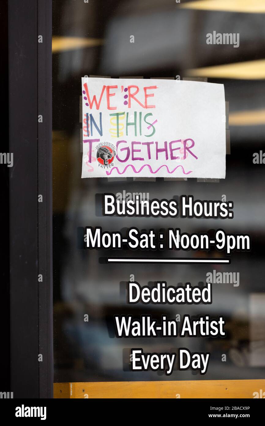 We’re In This Together paper sign on tattoo parlor window closed due to COVID-19. Stock Photo