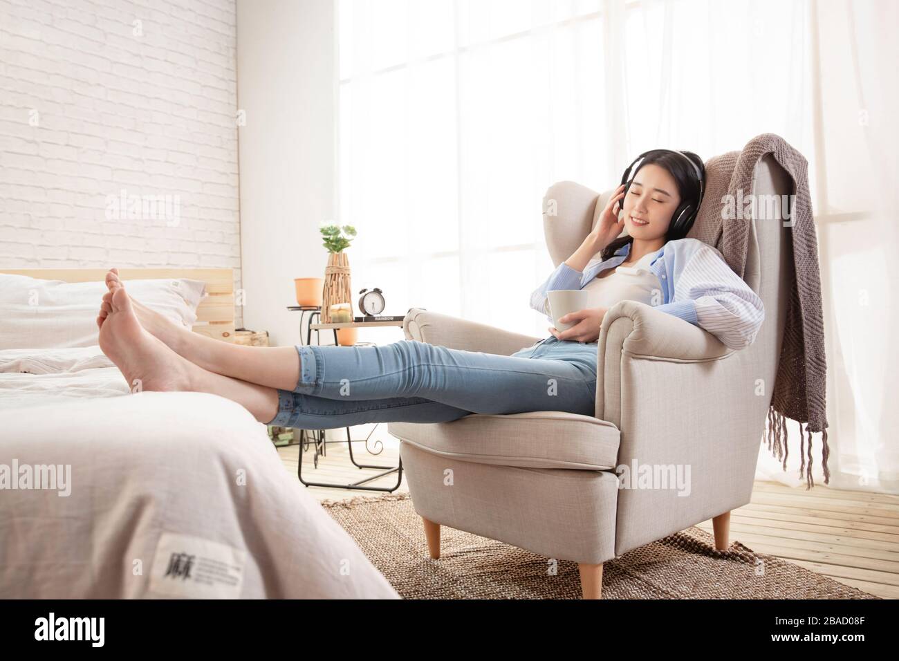 Happy young woman sitting on the sofa listening to music Stock Photo ...
