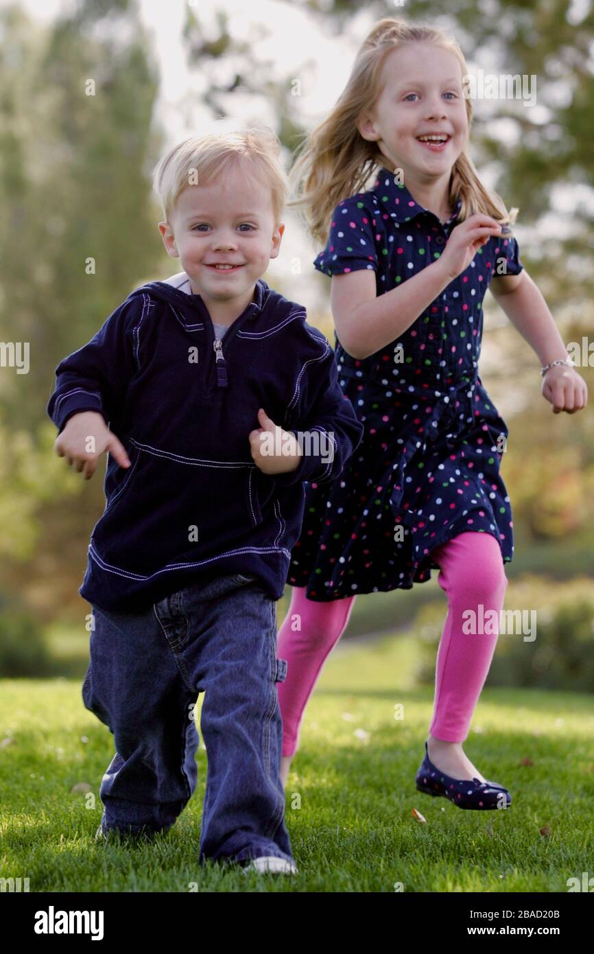 A young girl and boy run in a park having fun. Stock Photo