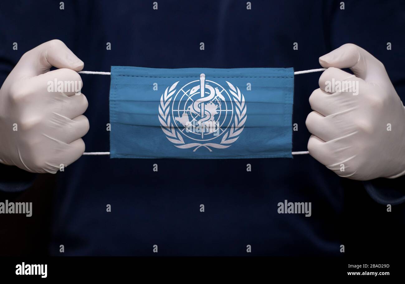 Health employee doctor holding medical face mask with WHO (World Health Organization) flag. Coronavirus (COVID-19) pandemic affects the country. Stock Photo