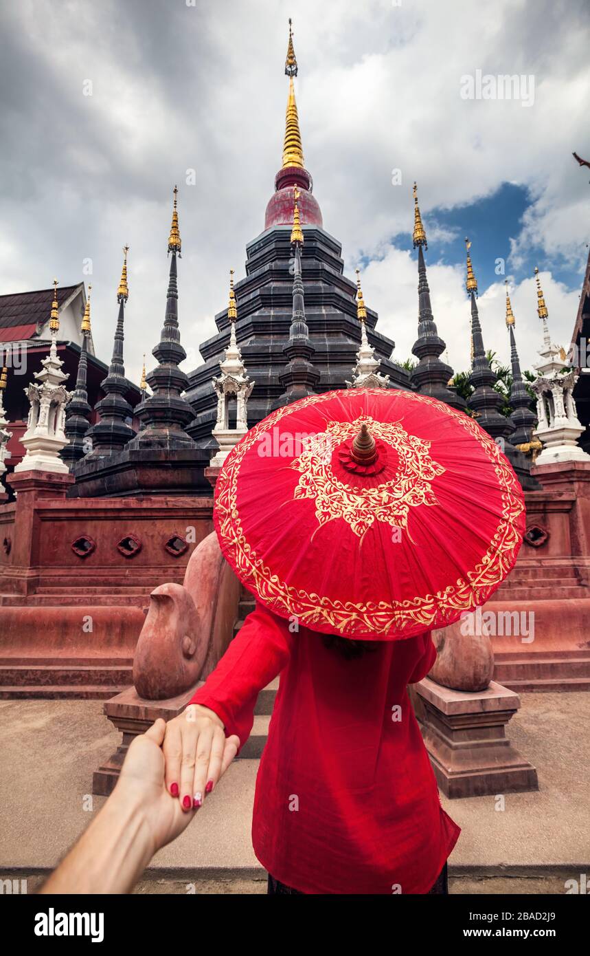 Woman with red traditional Thai umbrella holding man by hand and going to Black temple Wat Phan Tao in Chiang Mai, Thailand Stock Photo