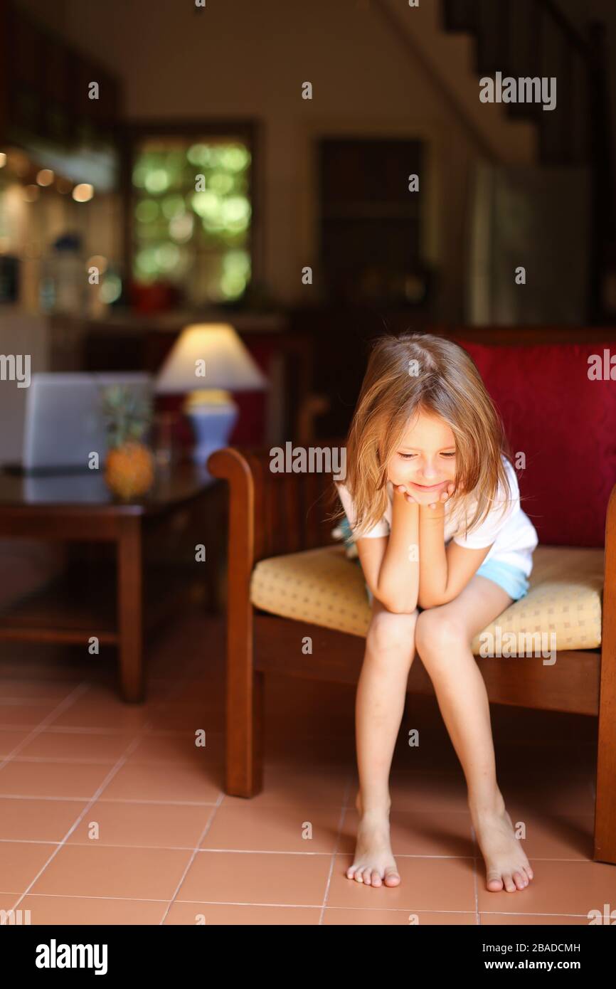 Little blonde girl sitting in wooden chair in living room Stock Photo ...