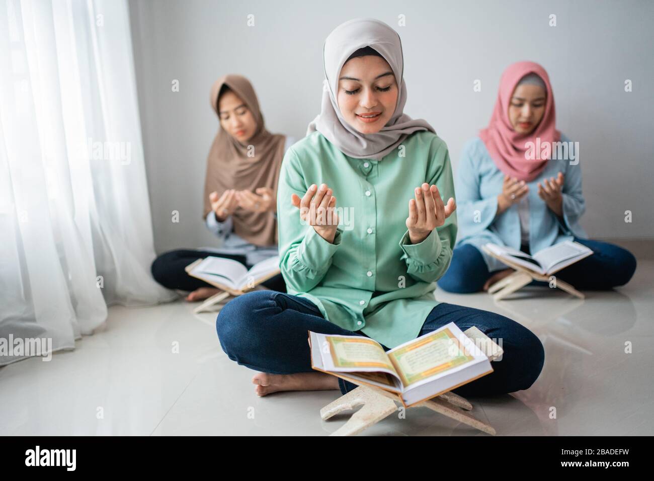 three Asian women sit and pray to give thanks to God while learning to recite the Holy Qur'an together in the house Stock Photo